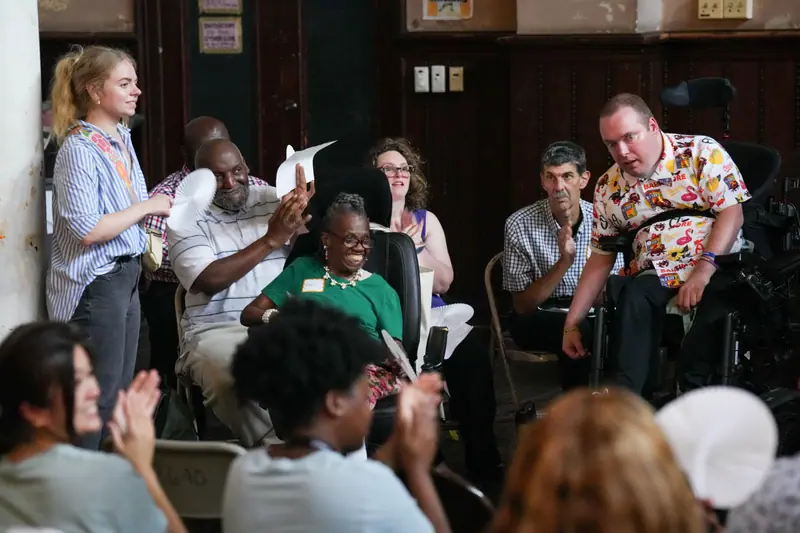 Storytellers and audience members applaud together at the Baltimore event, several holding printed scripts.